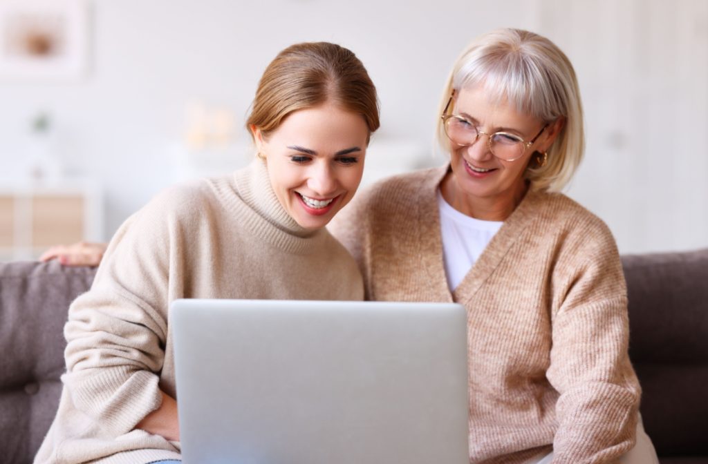 A young adult and their older parent side-by-side on the couch using a laptop to research independent and assisted living communities.