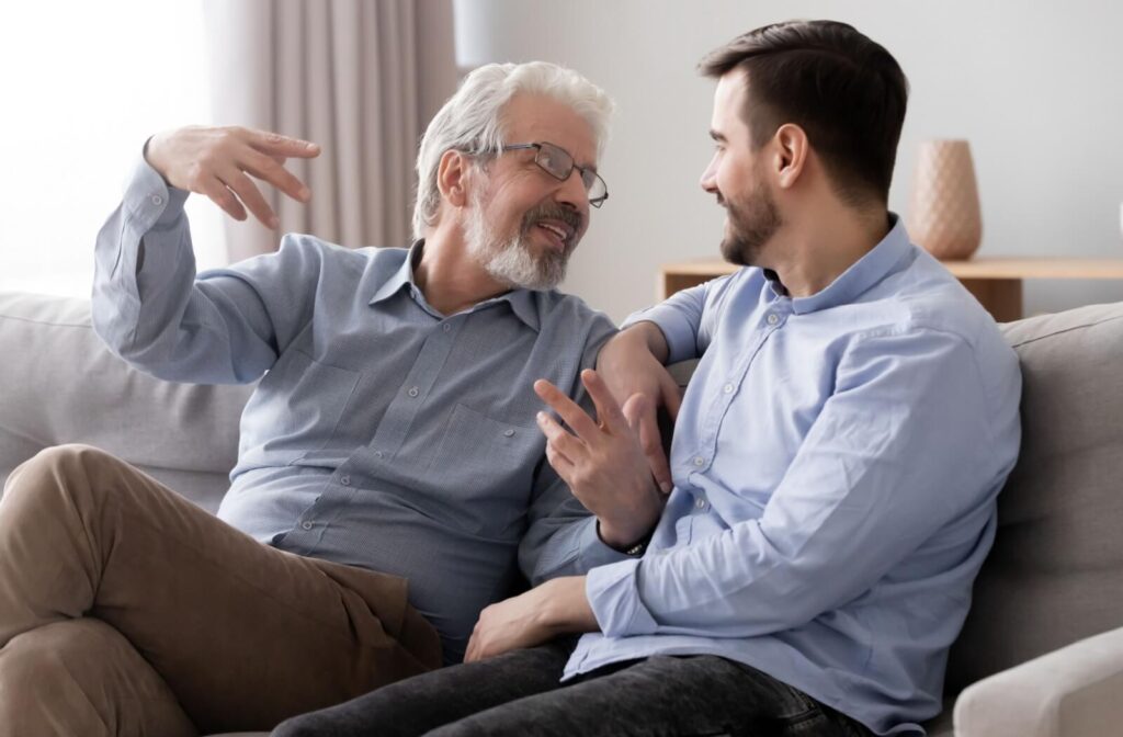 Smiling senior sits on a couch while talking with nonverbal gestures to their adult child.